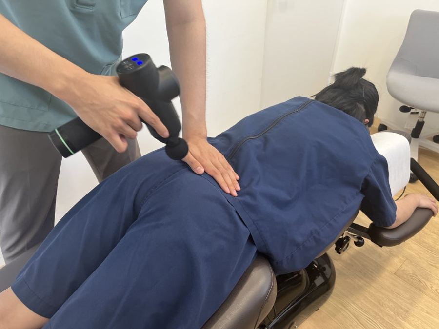 엎드린 환자의 허리에 마사지건을 대는 모습