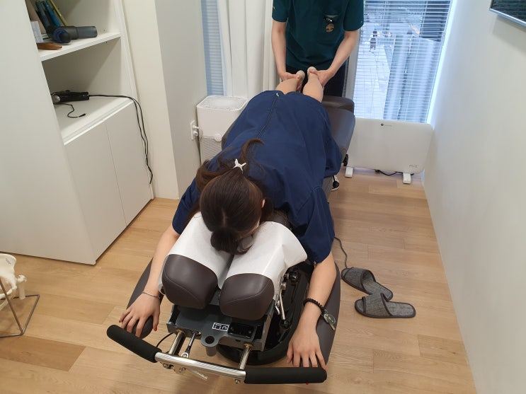 엎드린 환자의 발을 잡고 자세를 교정하는 치료 장면